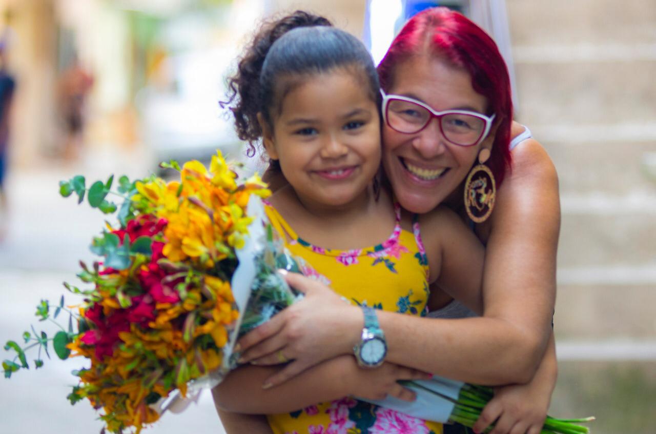 Mulher ruiva com óculos e criança abraçada com ramalhete de flores